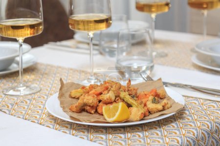 Photo for Deep fried seafood (fritomisto) on kraft paper served with a knife and fork with a glass of water and wine - Royalty Free Image