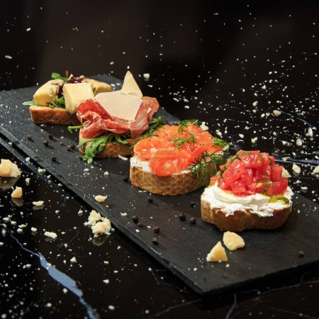 set of four bruschettas (camembert, tomatoes, salmon, jamon) served on a black marble table