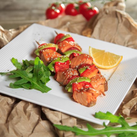 skewers of salmon, zucchini and tomato on a square plate on craft paper
