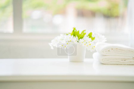Photo for White cotton towels with white flowers on a white counter table inside a bright bathroom background. For product display montage - Royalty Free Image
