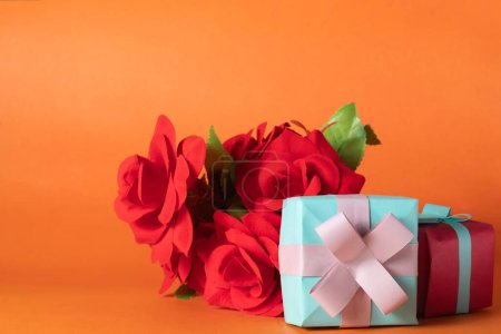 Bouquet of red roses and gift box on orange background. Valentines day concept.