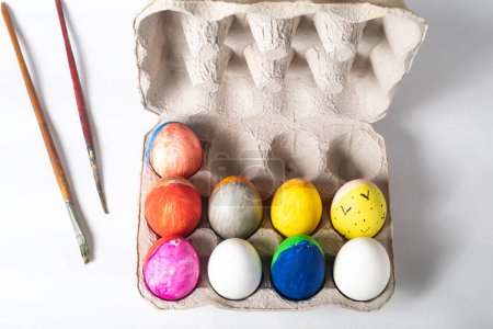 Photo for Easter eggs in a cardboard box and paint brushes on a white background, top view - Royalty Free Image