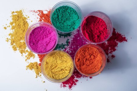Colorful holi powder in plastic containers on a white background. Top view