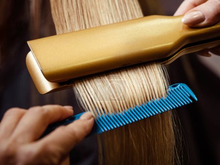 Foto de Peluquería usando un cabello alisado para alisar el cabello. Peluquero trabajando en el peinado de una mujer en el salón. - Imagen libre de derechos