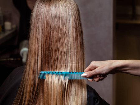 Foto de Peinate el pelo. Mujer joven peinándose el pelo con el pelo largo y rubio. - Imagen libre de derechos