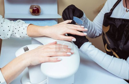 Nahaufnahme einer Frau in einem Nagelstudio, die von einer Kosmetikerin mit Nagelfeile eine Maniküre erhält. Frau bekommt Nagel-Maniküre.