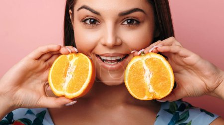 Téléchargez les photos : Jeune femme caucasienne tenant des fruits orange et souriant isolé sur fond rose. Concept de mode de vie sain - en image libre de droit