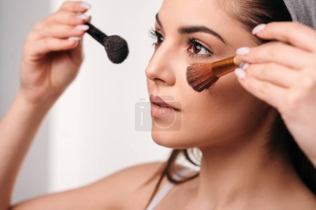 Photo for Gorgeous young woman with long hair smiling, posing, using makeup brushes for applying blush. Teenage girl doing her own makeup - Royalty Free Image