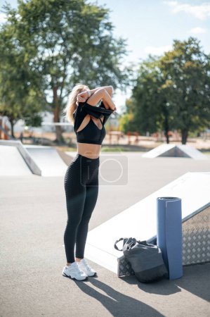 Foto de Vista vertical de la joven mujer quitándose la ropa mientras se prepara para el entrenamiento en la calle. Concepto de entrenamiento y deporte - Imagen libre de derechos