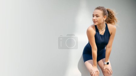Foto de Mujer deportiva rubia de pie cerca de la pared, mirando hacia otro lado y relajándose después de hacer ejercicio en la calle de verano. Concepto de personas y deporte - Imagen libre de derechos