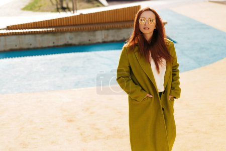 Photo for Hipster ginger woman wearing stylish clothes posing at the urban stadium background. Ginger girl in sunglasses standing at the street - Royalty Free Image