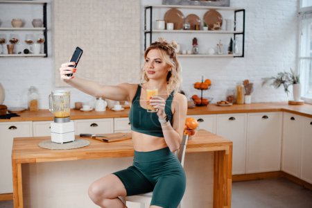 Photo for Blonde woman using mobile for filming video about healthy eating. Cute girl making selfie with orange juice glass - Royalty Free Image