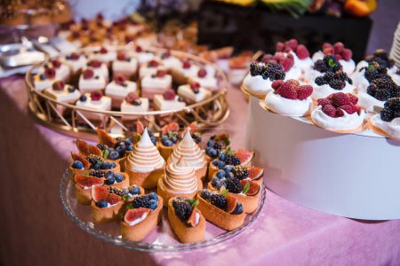 Téléchargez les photos : Tasty desserts with slices of passion fruit, seasonal berries fresh mint leaves served in festive table. Exotic candy bar for modern holiday event. - en image libre de droit