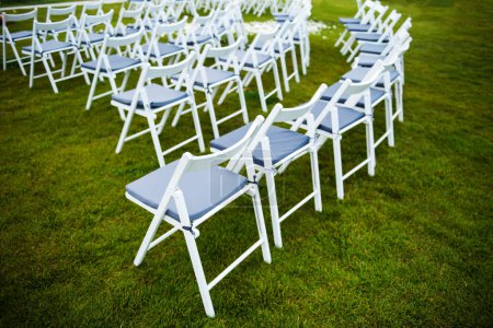 Photo for White wooden chairs standing in rows on green grass and prepared for wedding ceremony on fresh air. Places for guests on outdoor event. - Royalty Free Image