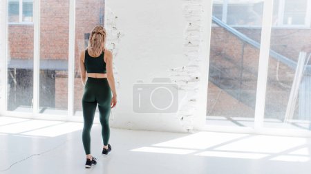 Photo for Back view of sporty young woman standing in white studio and looking to the window. Fitness and sport concept - Royalty Free Image