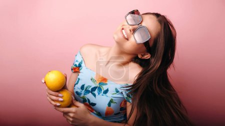 Téléchargez les photos : Jeune femme souriante en lunettes de soleil s'amusant tenant des oranges isolées sur fond rose. Concept d'émotions humaines - en image libre de droit