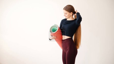 Téléchargez les photos : Femme de fitness souriante debout dans un studio de fitness portant un tapis de yoga. Portrait d'une jeune femme dans un centre d'entraînement physique. - en image libre de droit