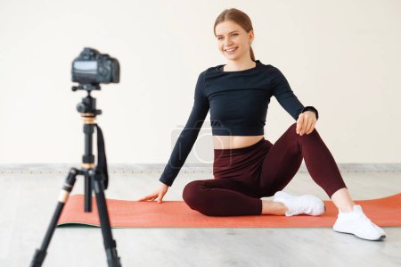 Foto de La blogger atlética en ropa deportiva dispara video en cámara en la clase de yoga. Concepto de deporte y recreación. Estilo de vida saludable. - Imagen libre de derechos