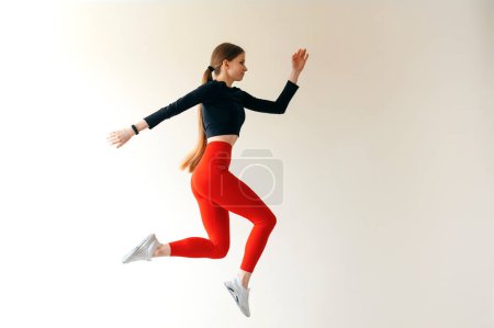 Foto de Mujer atlética caucásica vestida con ropa deportiva elegante y con cola de caballo saltando. En la pared de fondo. Copiar espacio - Imagen libre de derechos