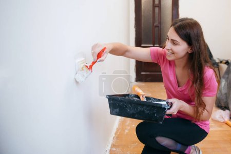 Foto de Joven mujer sonriente pintando paredes con un rodillo en una casa nueva. Diseño de interiores. Renovación - Imagen libre de derechos