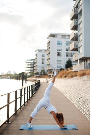 Foto de Tiro vertical de mujer joven en forma haciendo ejercicio de estiramiento cerca del río. Modelo Fitness Ejercicio en la mañana al aire libre - Imagen libre de derechos