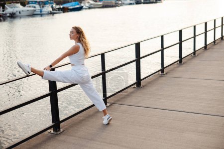 Foto de Mujer joven mirando a la distancia y estirando las piernas cerca del río. Modelo Fitness Ejercicio en la mañana al aire libre - Imagen libre de derechos