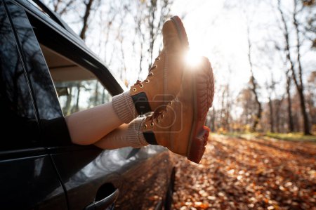 Téléchargez les photos : Vue recadrée des jambes de la femme depuis la fenêtre automatique pendant la journée d'automne. Voyage en forêt d'automne en voiture concept - en image libre de droit