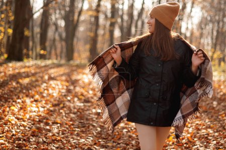 Photo for Photo of positive cheerful girl enjoy autumn weather wrapping in blanket and looking away in forest or park full of leaves - Royalty Free Image