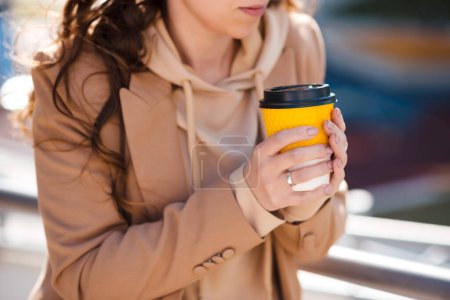 Foto de Primer plano de las manos femeninas con taza de café amarillo. Soleado día de primavera al aire libre. - Imagen libre de derechos
