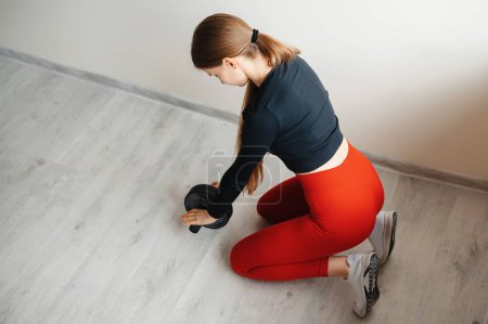 Photo for Above view of determined female sitting on knees and exercising with dumbbells on floor of training studio. Healthy woman performing workout practice indoors. Concept of fitness and sport. - Royalty Free Image