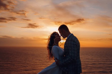Photo for Silhouette of a loving couple at sunset, with sea background. Bride and groom looking at each other. Concept of family, wedding, and honeymoon. - Royalty Free Image