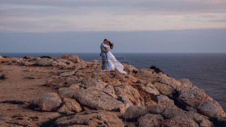 Téléchargez les photos : Doux jeune couple de mariage, mariés, marche et câlin sur une plage rocheuse près de la mer le soir Chypre. Belle séance photo de mariage. Mariage pour deux, temps pour deux
. - en image libre de droit