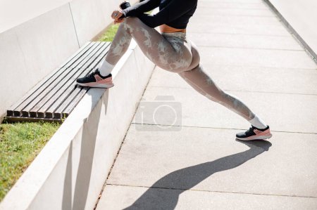 Téléchargez les photos : Cropped view of the strong sportswoman in training clothes warming up and doing stretch exercises at the street in summer day morning. Sport concept - en image libre de droit