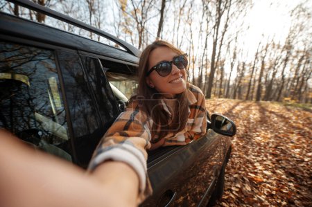 Téléchargez les photos : Pov de la femme faisant selfie à partir de la fenêtre de la voiture pendant le road trip d'automne. Voyage en forêt d'automne en voiture concept - en image libre de droit