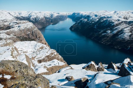 Foto de Paisaje escénico de lago entre costa rocosa con nieve. Vista superior de la roca del púlpito, Preikestolen. Montañas noruegas. Lysefjord, Noruega - Imagen libre de derechos