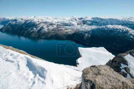 Foto de Hermosa vista del lago con la costa rocosa con montañas con picos nevados. Vista superior de la roca del púlpito, Preikestolen. Lysefjord, Noruega - Imagen libre de derechos