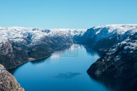 Foto de Paisaje escénico de lago con la costa rocosa con montañas con picos nevados. Vista superior de la roca del púlpito, Preikestolen. Lysefjord, Noruega - Imagen libre de derechos