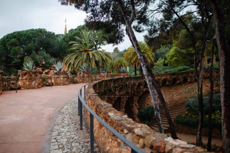 Foto de Road over stone columns in botanical garden of Spain. Spire of Gaudi museum visible through beautiful plants, palms and trees. - Imagen libre de derechos