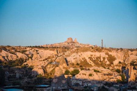 Téléchargez les photos : Beau paysage de village turc dans la région de Cappadoce au milieu des montagnes rocheuses. Ciel bleu sans nuages. Concept d'été et de voyage. - en image libre de droit