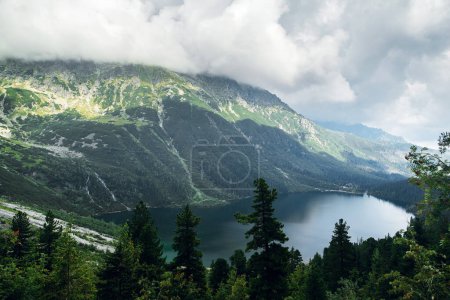 Téléchargez les photos : Vue de dessus des collines verdoyantes et des montagnes dans les nuages sombres et réflexion sur le lac Marine Eye, Hautes Tatras, Zakopane, Pologne. Foggy day - en image libre de droit