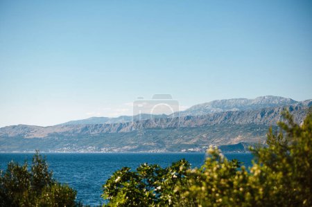 Téléchargez les photos : Arbres verts avec vue panoramique sur la côte de l'île de Brac. Paysage fascinant de belle mer Adriatique claire et de hautes montagnes rocheuses. Atmosphère de calme. - en image libre de droit