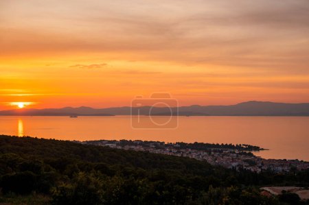 Téléchargez les photos : Ciel orange et doré au coucher du soleil sur la ville de Supetar en Croatie. Panorama spectaculaire sur le paysage urbain et la mer calme. Bel horizon avec vue panoramique sur la côte. Vacances au bord de la mer. - en image libre de droit