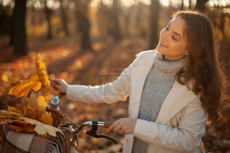 Photo for Portrait of the woman standing with bicycle in forest in autumn at sunset. Colourful landscape with girl around trees with orange leaves in fall. Travel concept - Royalty Free Image