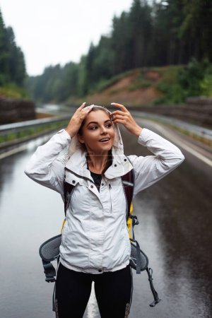 Photo for Attractive young woman in raincoat with backpack hiking among mountains during foggy weather. Pretty brunette enjoying outdoors activity alone. - Royalty Free Image