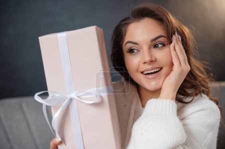 Téléchargez les photos : Portrait de la femme surprise posant avec des boîtes cadeaux alors qu'elle était assise sur le canapé. Noël vacances concept - en image libre de droit