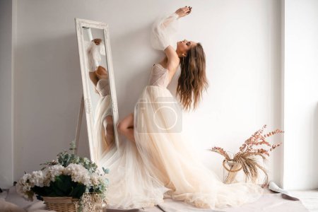 Foto de Beautiful dress. Full length of attractive young woman wearing wedding dress standing in front of the mirror in bridal shop. Stock photo - Imagen libre de derechos