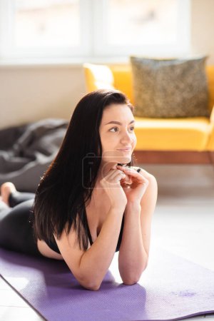 Photo for Portrait of attractive woman with dark long hair relaxing on yoga mat after workout. Healthy young female in activewear - Royalty Free Image