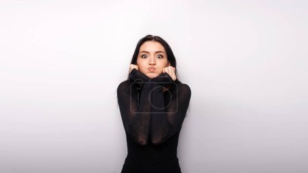 Foto de Portrait of funny crazy woman standing and looking with big eyes and fish lips, having fun, humour, wearing casual style clothes. Indoor studio shot isolated on white background - Imagen libre de derechos