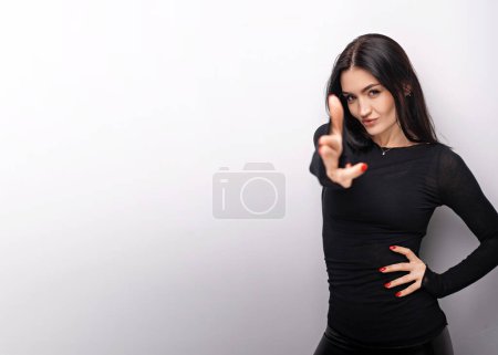 Téléchargez les photos : Female in casual clothes pointing finger pistol to camera, threatening to shoot, looking displeased angry and dangerous. Indoor studio shot isolated on white background - en image libre de droit
