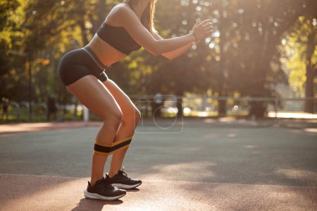 Téléchargez les photos : Des squats. Croped vue de sport femme dans la mode vêtements accroupi avec bande de plein air - en image libre de droit
